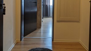 Een gang met een houten vloer, een zwart tapijt, een deur naar een andere kamer en een klein plankje met een vaas.