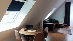 Een eetruimte met een ronde tafel, vier stoelen en een bijzettafeltje met een glas. Achtergrond toont een bank en een salontafel.