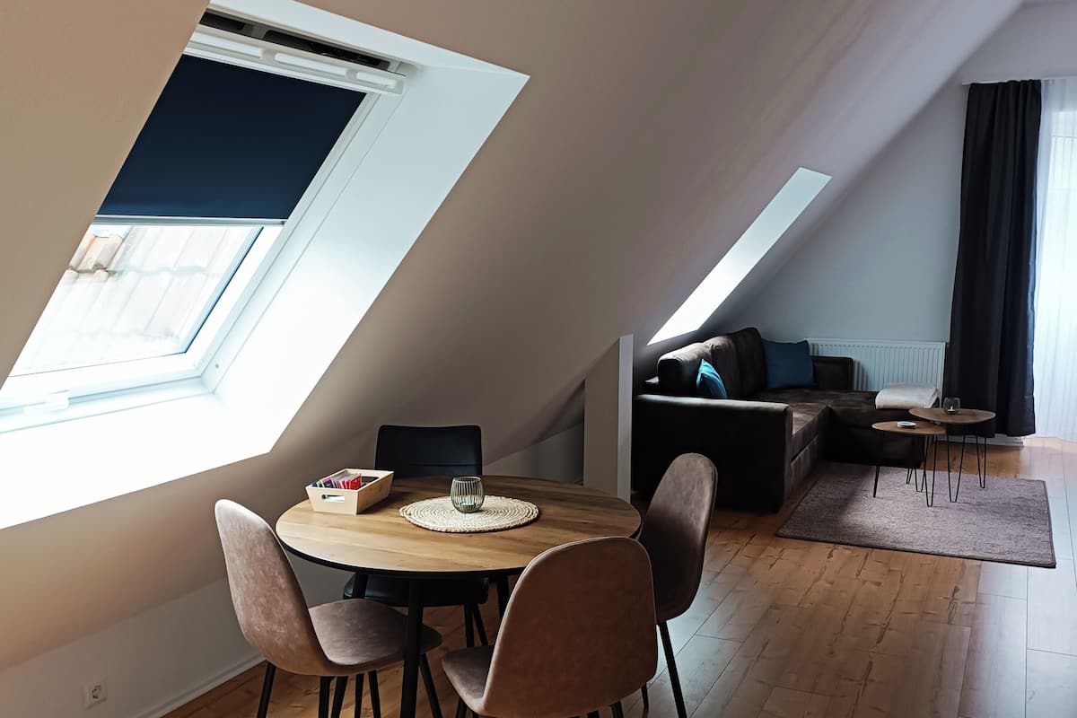 Un coin repas avec une table ronde, quatre chaises et une petite table d’appoint avec un verre. On aperçoit un canapé et une table basse à l’arrière-plan.