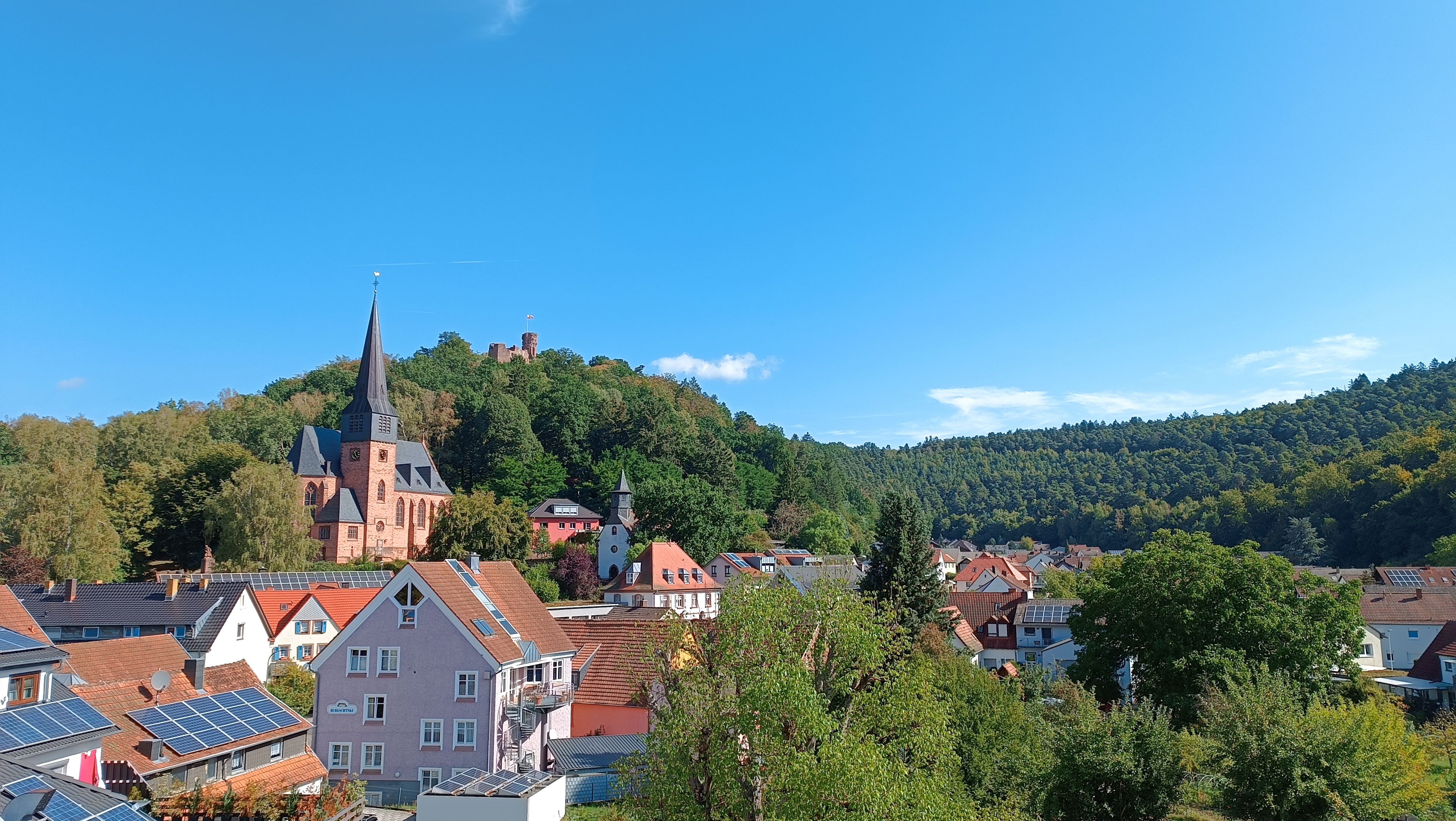 A town with a prominent church on a hill, surrounded by residential buildings and lush greenery.