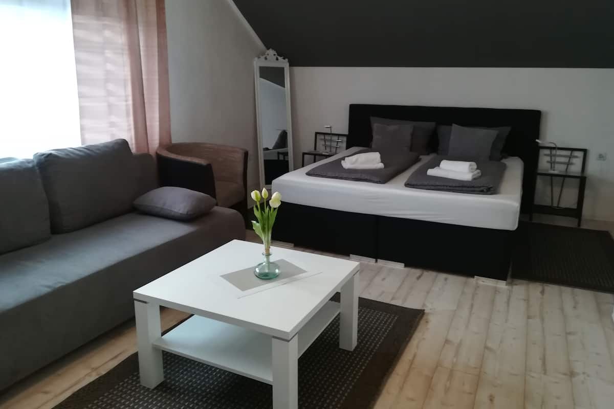 Une chambre à coucher moderne avec un lit, une table de chevet, un miroir, un canapé et une petite table sur laquelle est posé un vase.