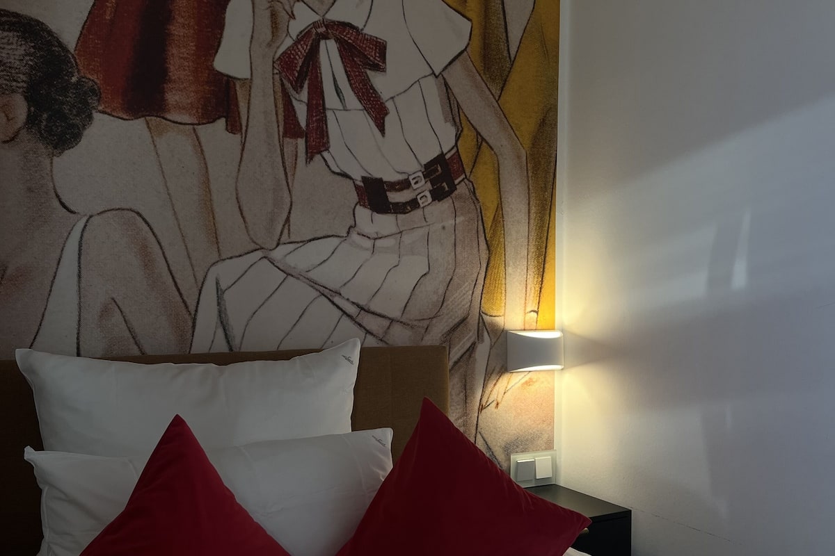 Een hotelkamer met een bed, kussens en een muurschildering.