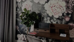 Een kamer met een grote bloemenmuur, een grijze bank en een houten bijzettafeltje met een plant.