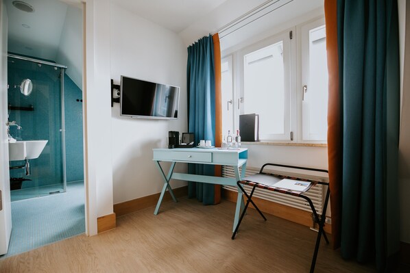 A hotel room with a shower, a desk with a computer, a radiator, and a window with curtains.