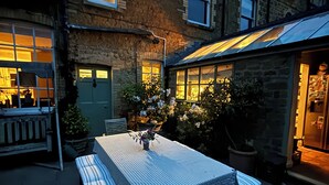 An outdoor patio with a table and benches, surrounded by stone buildings with large windows and a shop entrance. - Ellesmere House (Castle Cary)