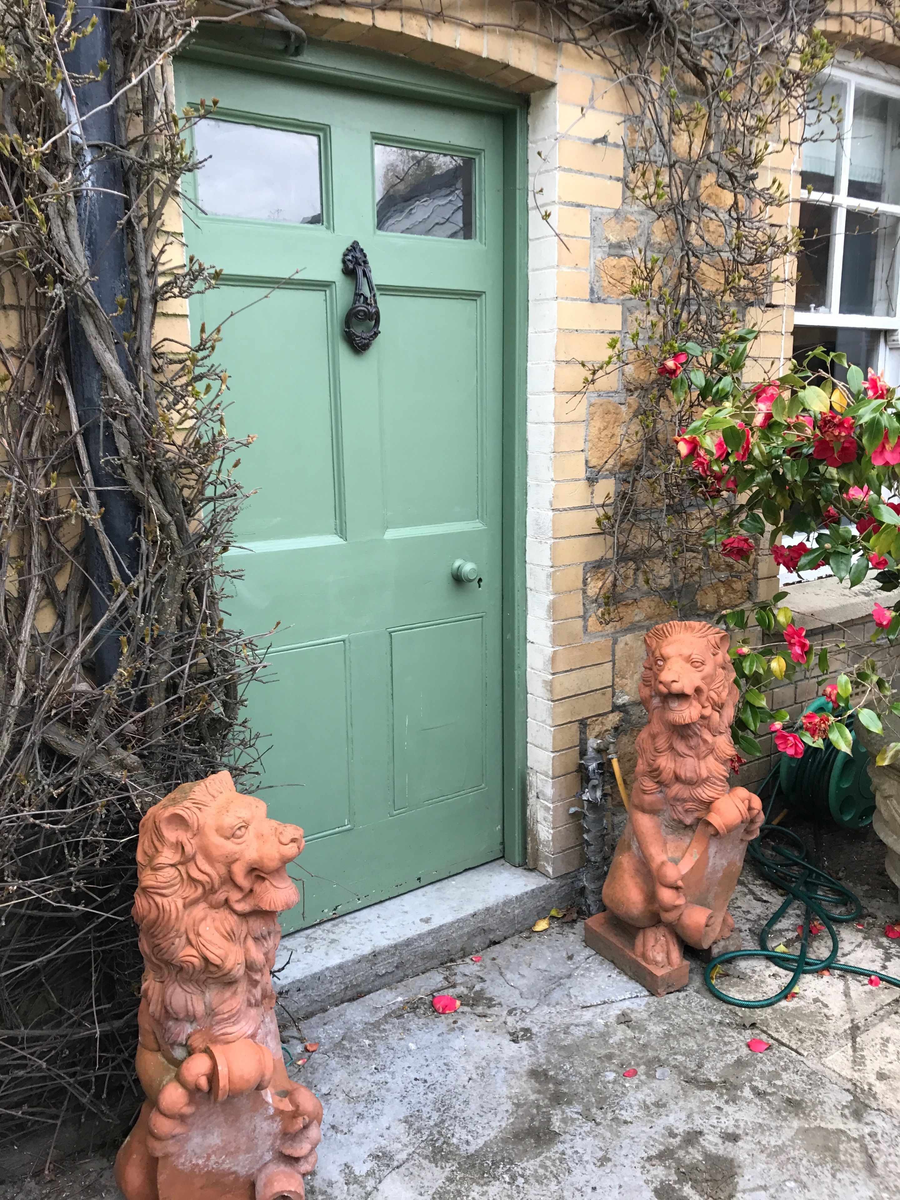 A green door with a lion statue on the left and a flower pot on the right.