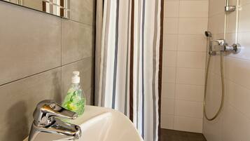 A bathroom with a shower, a sink, and a bottle of liquid soap.