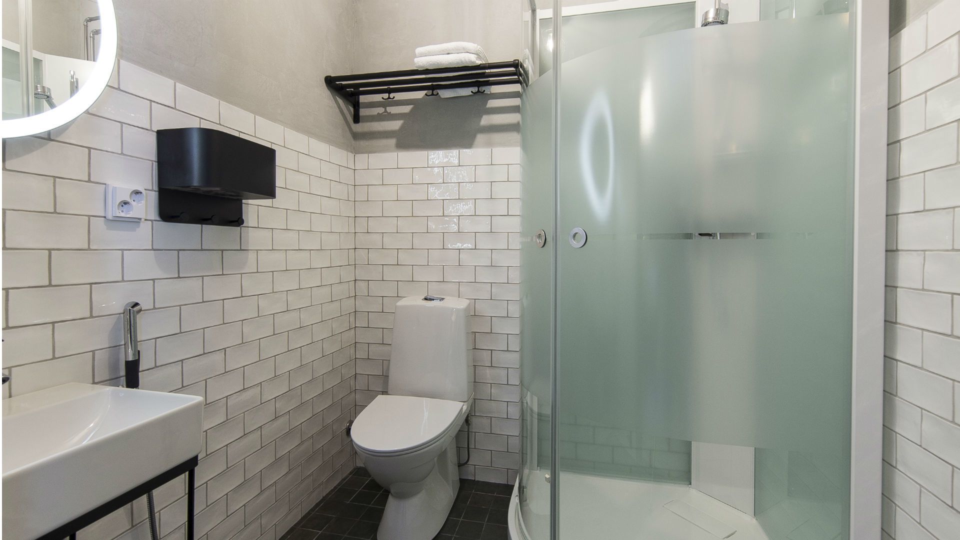 A modern bathroom with white subway tiles, a toilet, a sink, and a glass-enclosed shower.