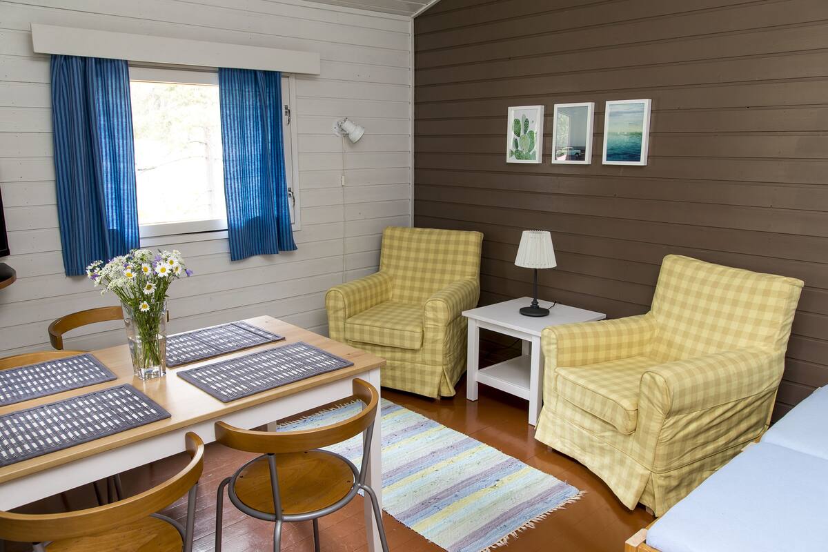 Um quarto acolhedor com uma mesa de madeira, duas poltronas xadrez, uma mesa pequena branca e um abajur.