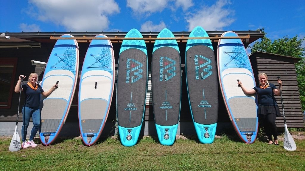 Sechs Aqua Marina Stand-Up-Paddles sind vor einem Gebäude aufgereiht.