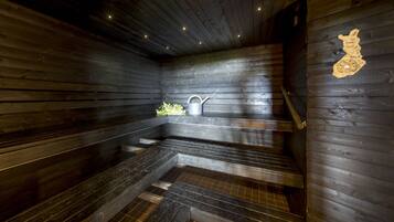 A sauna with wooden walls and steps, a bucket, and a wall-mounted heater.