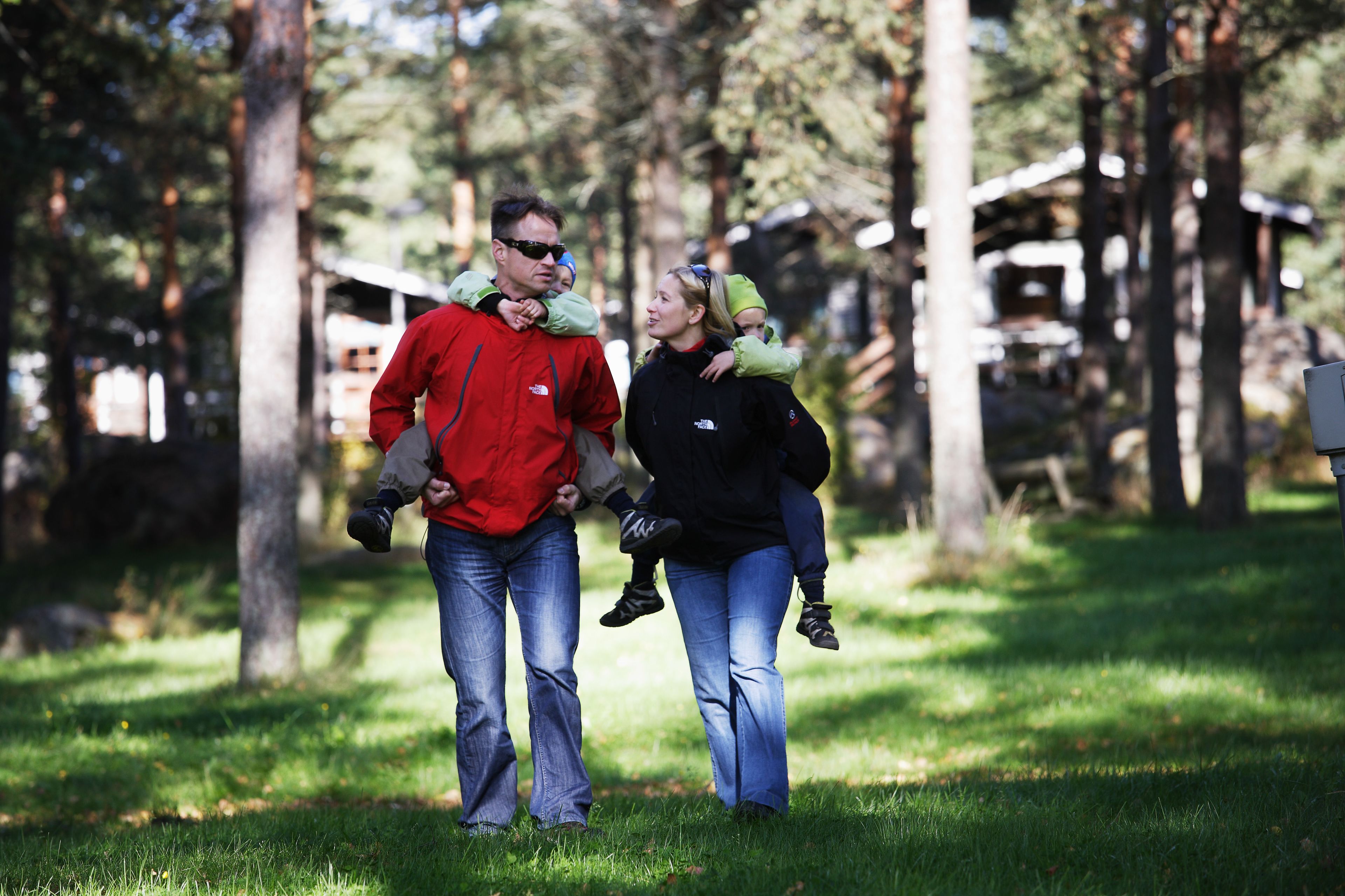 A family walking in a park with trees and a building in the background.