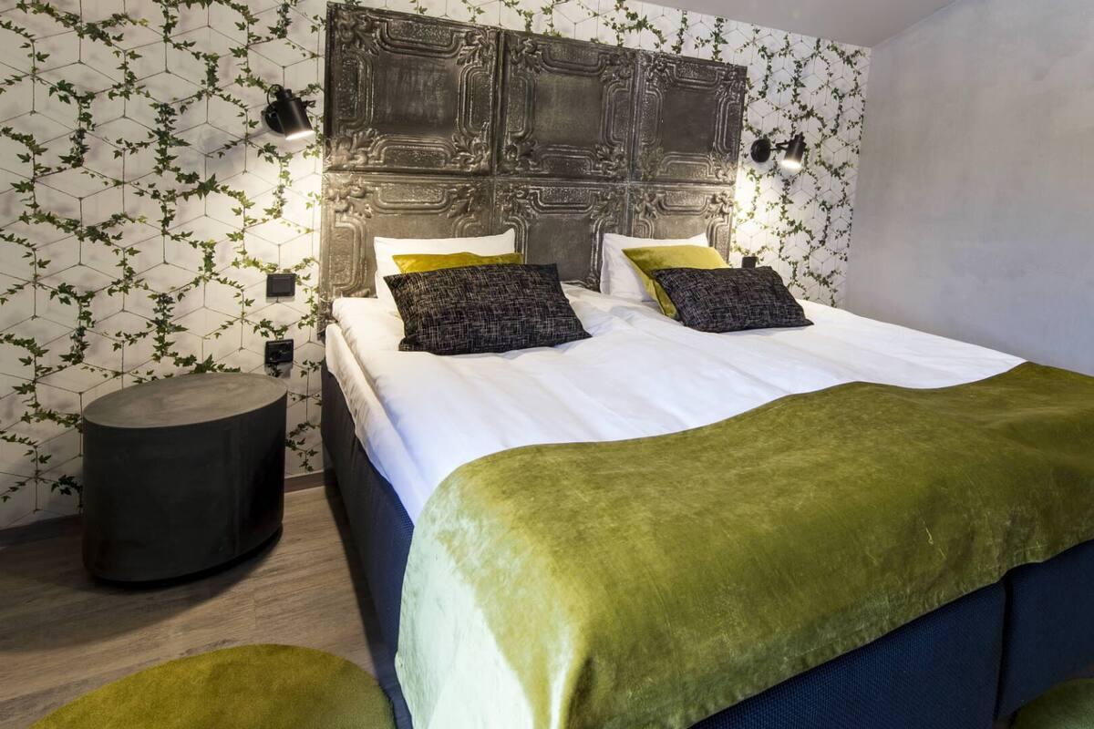 Quarto moderno com uma cama grande, cabeceira decorativa e mesa lateral redonda.