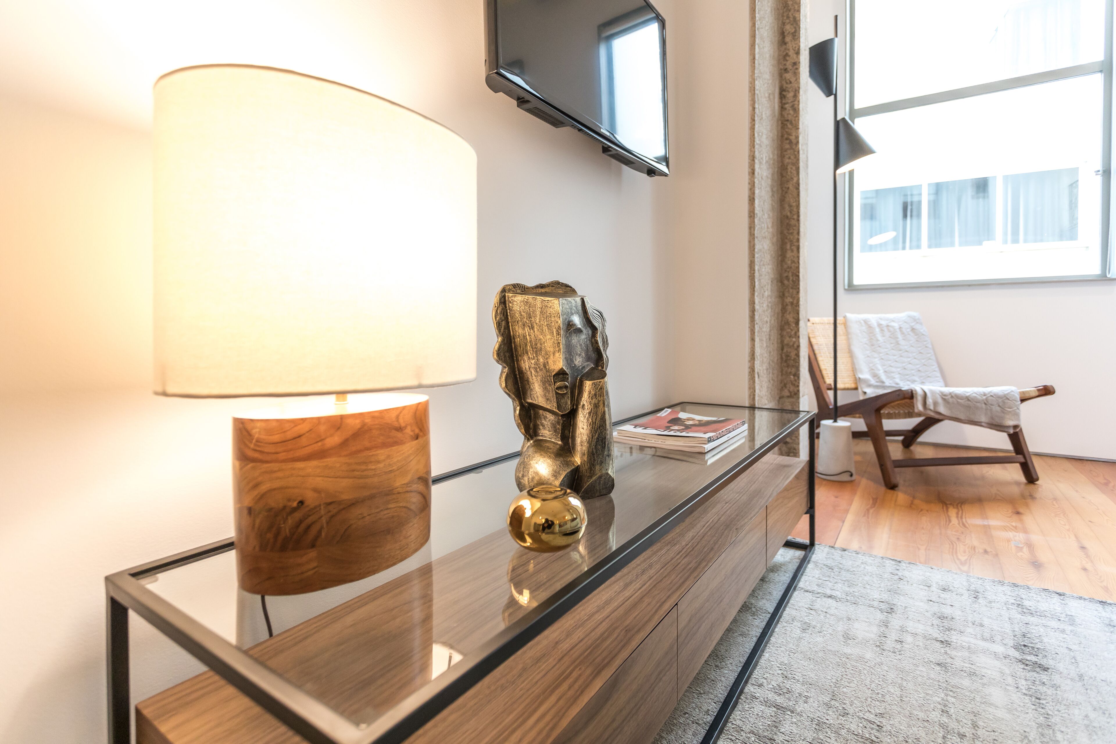 A modern room with a wooden desk, a lamp, a decorative sculpture, a chair, and a flat-screen TV mounted on the wall.