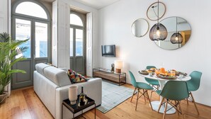 A modern living room with a sofa, dining table, chairs, and a TV. - Villa Bolhão Apartamentos (Porto)