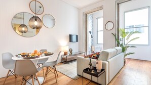 A modern living room with a dining area, featuring a sofa, chairs, a coffee table, and a dining table set for a meal. - Villa Bolhão Apartamentos (Porto)