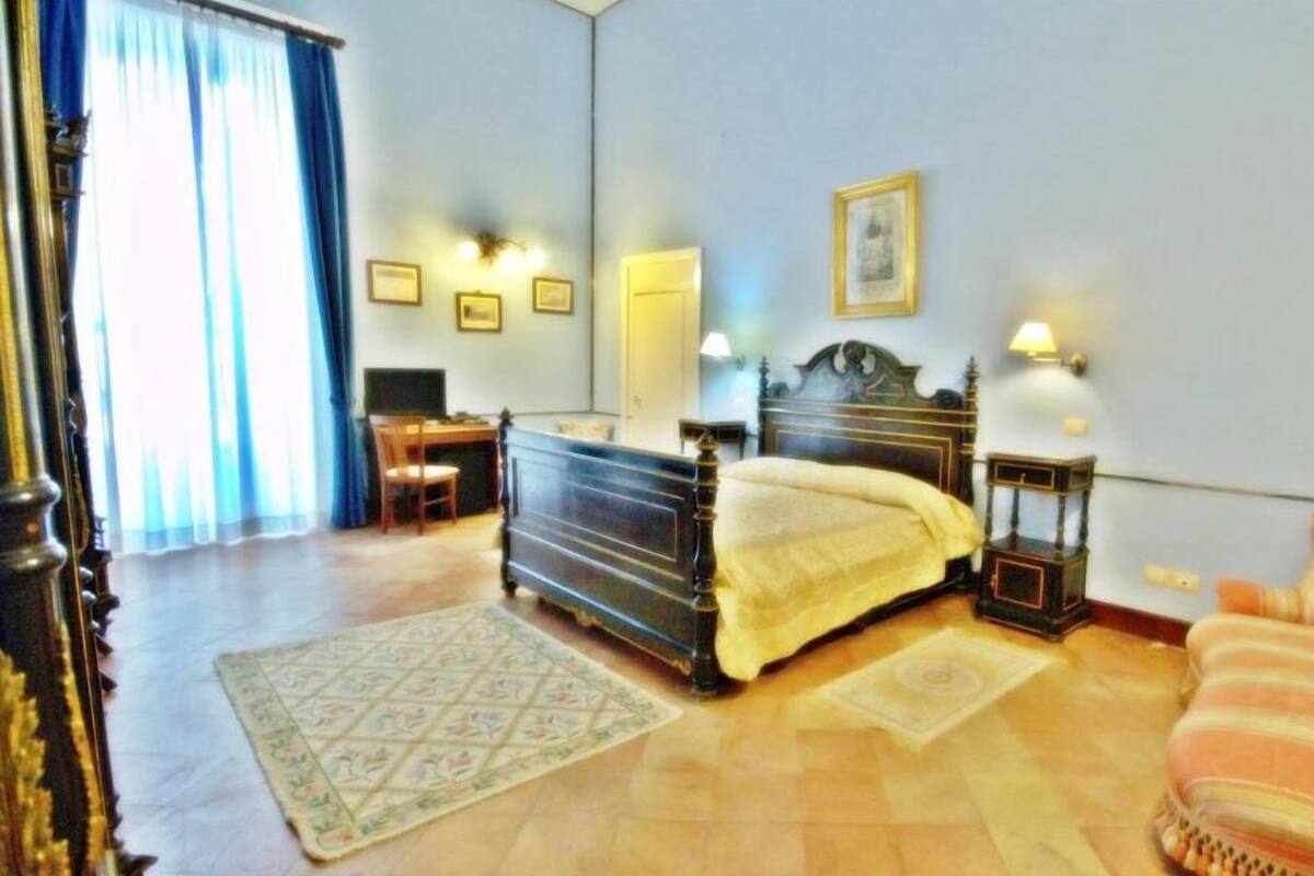 A bedroom with a bed, a desk, a chair, a lamp, and a window with curtains.
