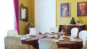 A dining room with a round table set for six, white chairs, a chandelier, and paintings on the walls. - B&B Casa Cavalli (Lucera)