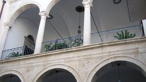 A building with multiple arches and columns, a balcony with metal railings, and hanging lanterns. - B&B Casa Cavalli (Lucera)