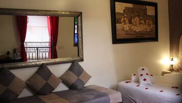 Una habitación de hotel con sofá, cama con pétalos de rosa, un espejo grande y un cuadro en la pared.