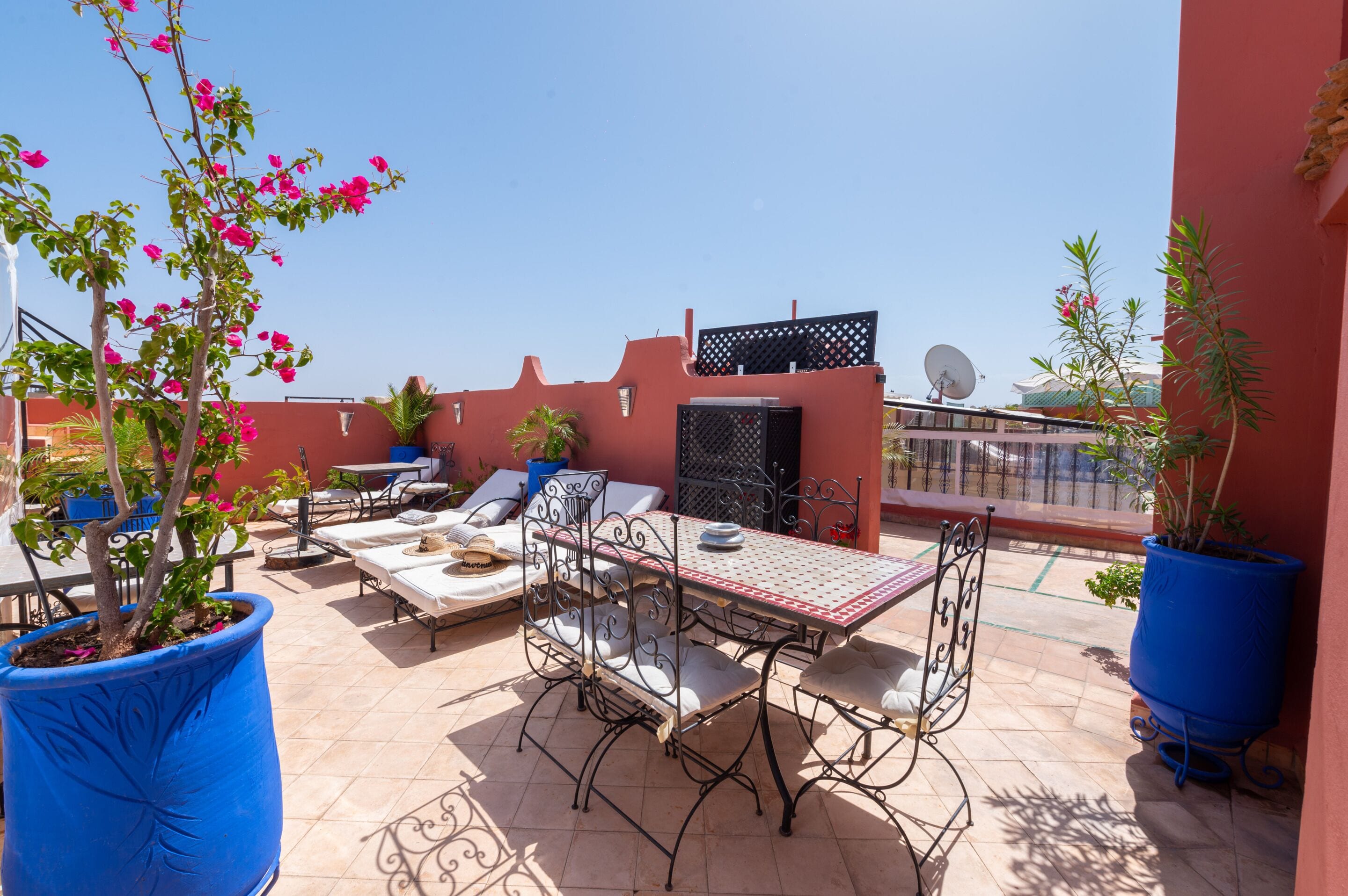 Una terraza en la azotea con una mesa, sillas, plantas en macetas y vistas de la ciudad.
