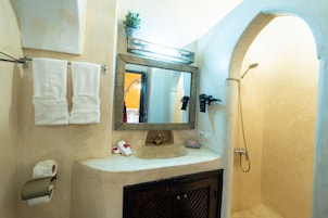 Un baño con lavamanos, espejo, toallero, ducha y papel higiénico.