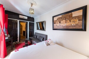 Habitación de hotel con cama, escritorio, sillón, sofá, cortina roja y un cuadro en la pared.