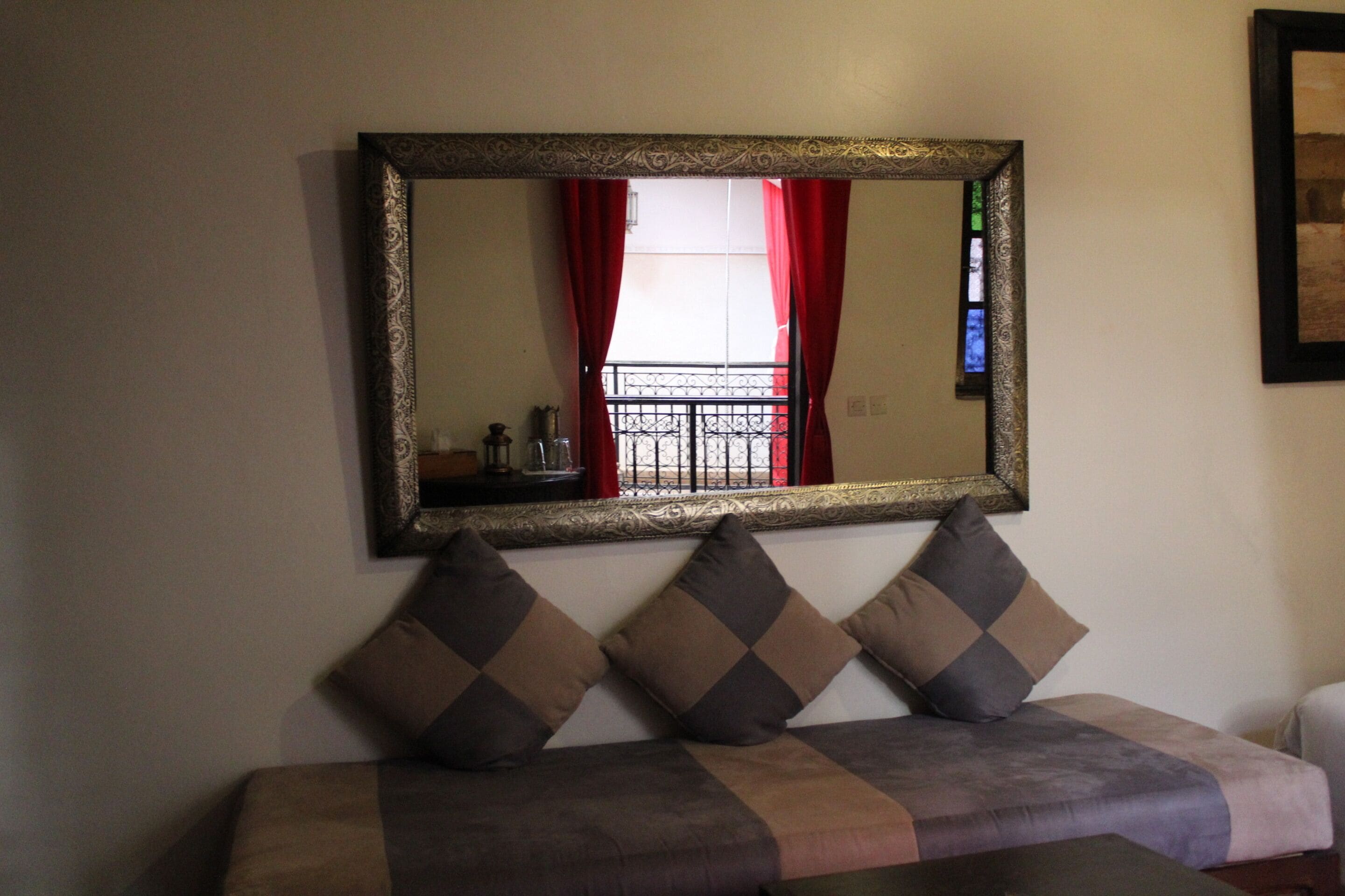 Una habitación con sofá, un espejo grande y una ventana con cortinas rojas.