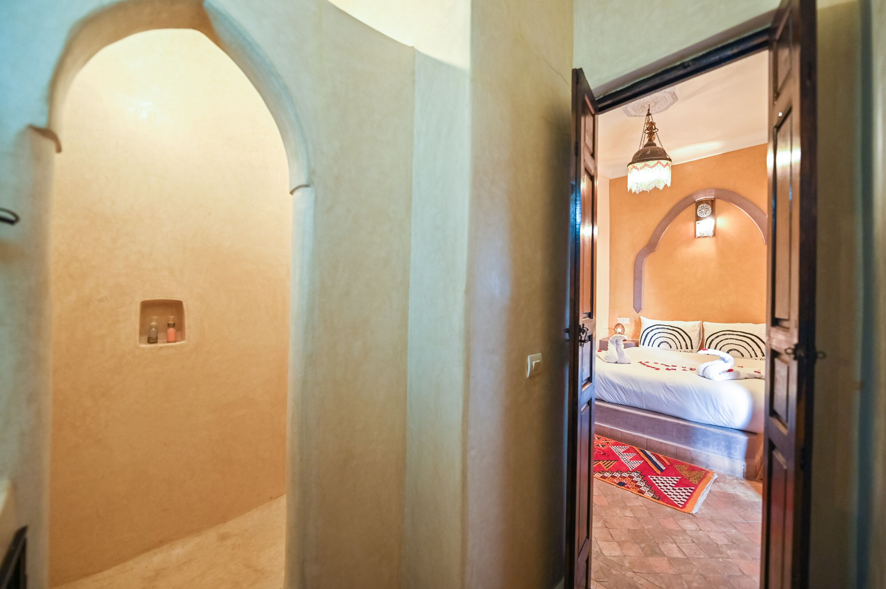 Un corridoio che conduce a una camera da letto con un letto, un lampadario e un tappeto decorato.