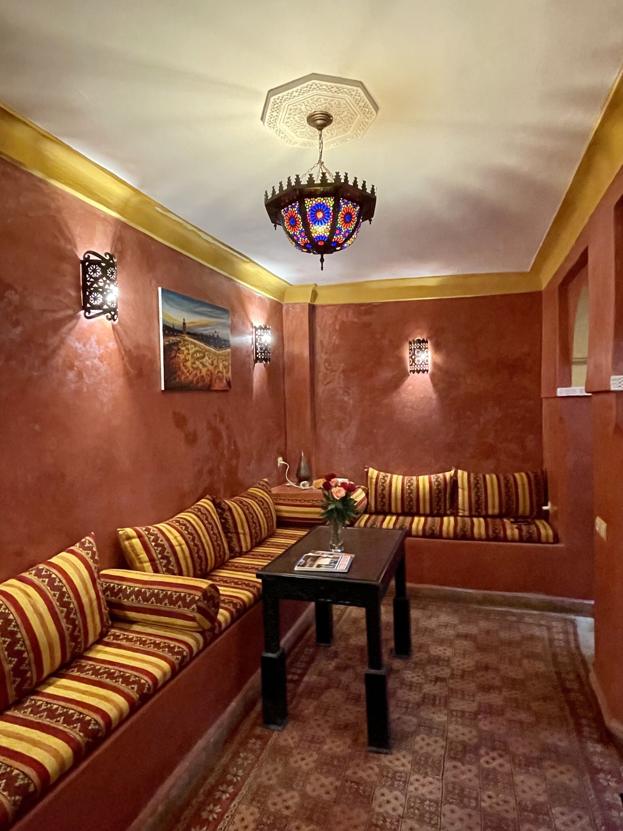 Ein Zimmer mit einer gemusterten Couchgarnitur, einem kleinen Tisch mit einer Vase und einer dekorativen Deckenleuchte.