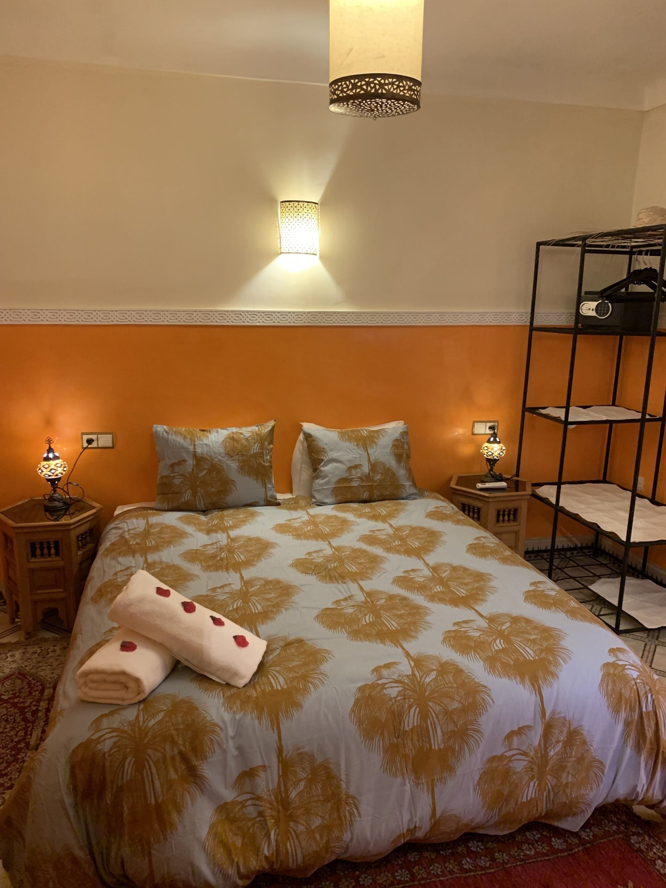 Quarto de hotel com uma cama, duas luminárias de cabeceira, uma luz na parede, uma cama beliche e um edredom estampado.