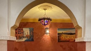 Un rincón acogedor con sofá y una mesa, una lámpara decorativa en el techo, y dos cuadros enmarcados en las paredes.
