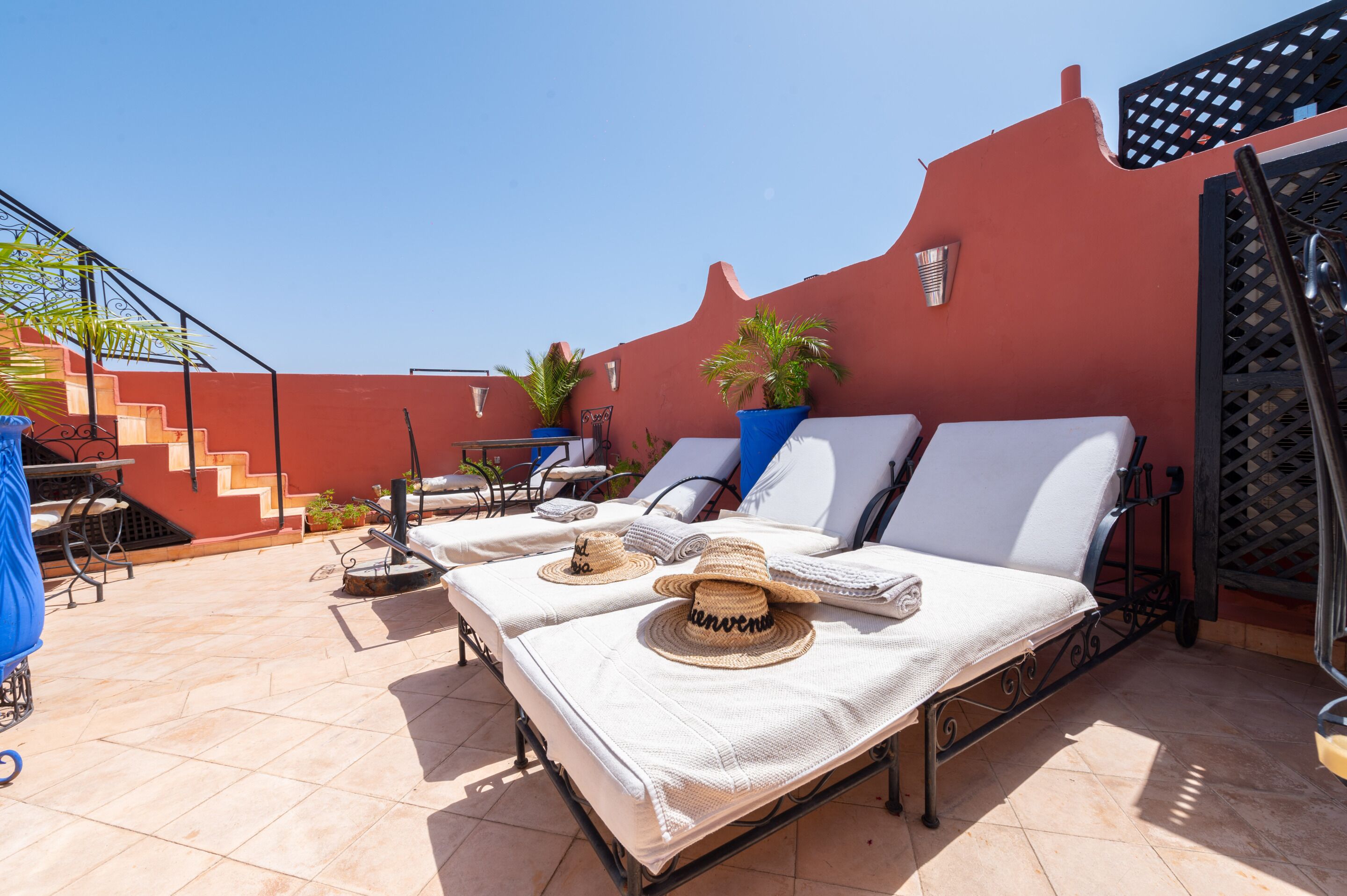 A rooftop terrace with two sunbeds, a table, chairs, and potted plants.