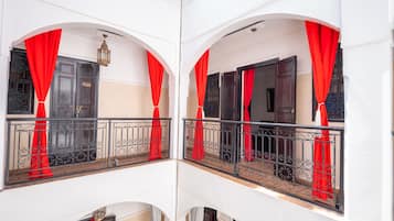 A balcony with red curtains, a black metal railing, and a white wall.