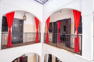 Un balcone con tende rosse, ringhiera in metallo nero e parete bianca.