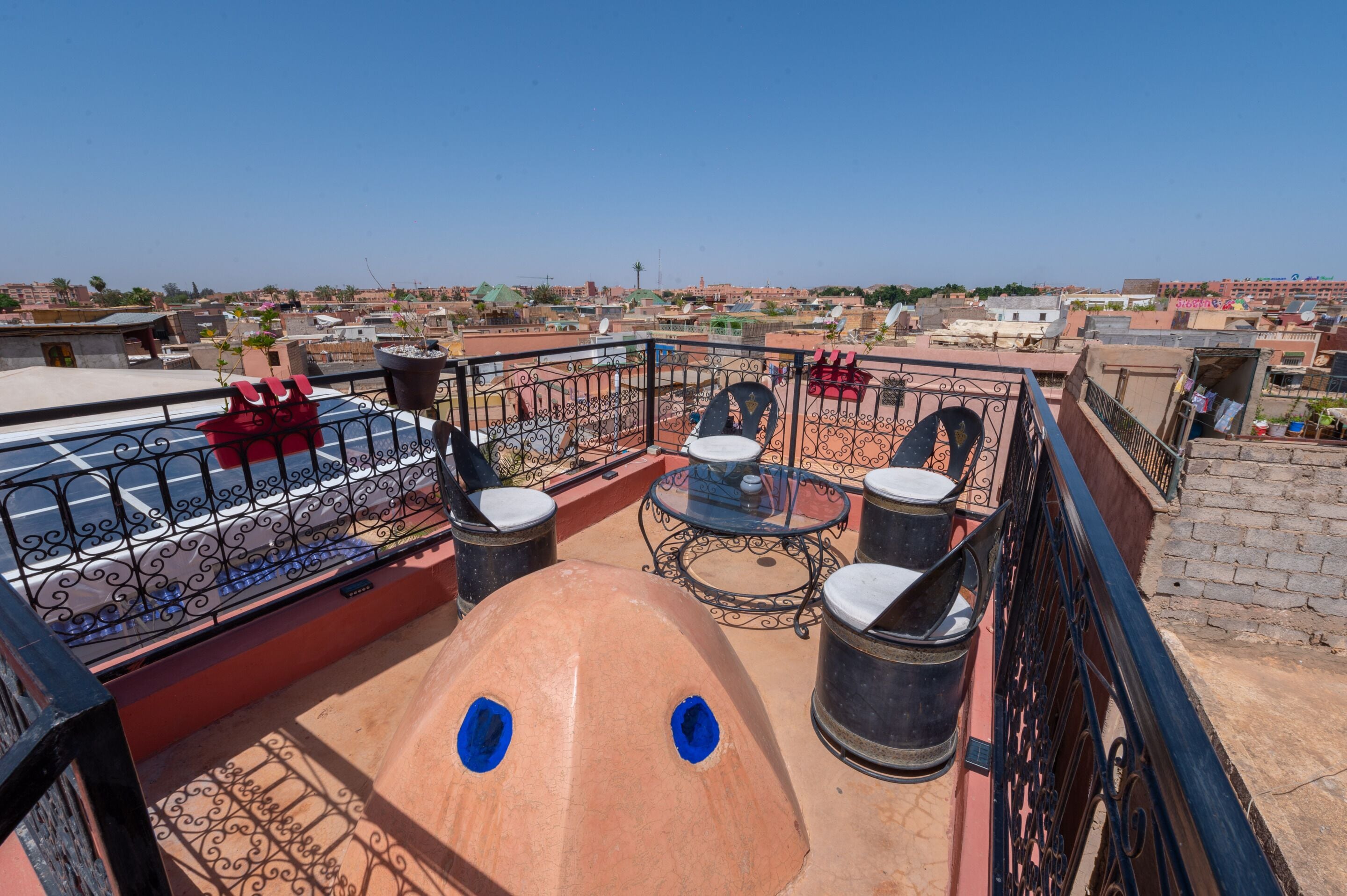 A rooftop terrace with a table and chairs, a red sofa, and a view of the cityscape.