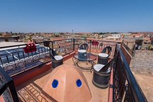 Una terraza en la azotea con mesa y sillas, un sofá rojo y vistas de la ciudad.