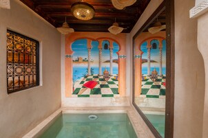 Zona de piscina con suelo a cuadros, un tapete rojo y un espejo decorativo que refleja una escena pintada.