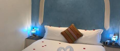 Una habitación de hotel con una cama grande, una pared azul decorativa y una disposición de toallas con forma de corazón sobre la cama.