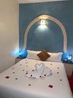 Una habitación de hotel con una cama grande, una pared azul decorativa y una disposición de toallas con forma de corazón sobre la cama.