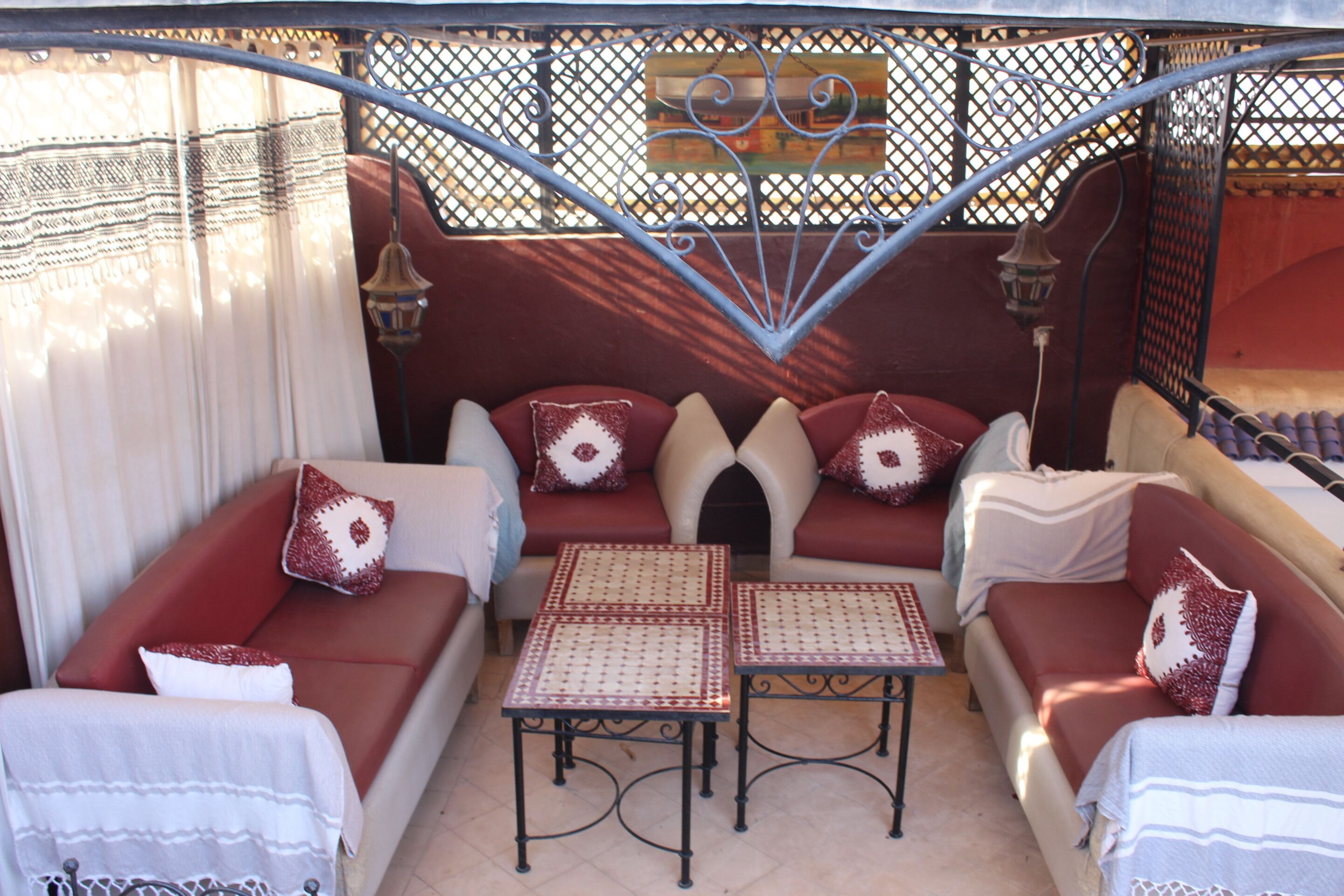 A cozy outdoor seating area with red sofas and patterned cushions, surrounded by a decorative metal fence and a tiled floor.