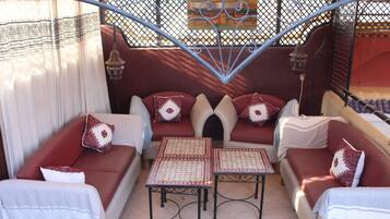 A cozy outdoor seating area with red sofas and patterned cushions, surrounded by a decorative metal fence and a tiled floor.