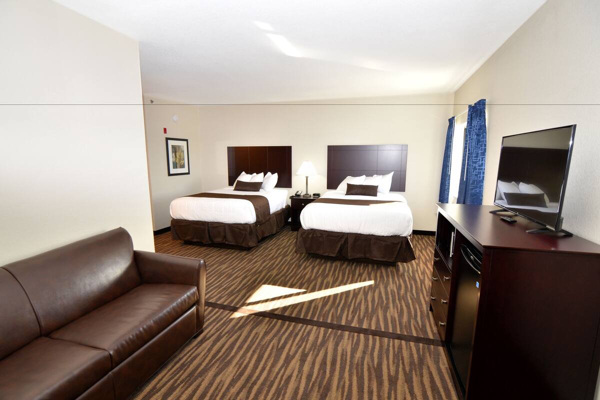 A hotel room with two beds, a sofa, a TV, and a desk.