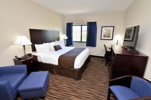 A hotel room with a large bed, two bedside tables with lamps, a desk with a chair, a television, and a window with curtains.