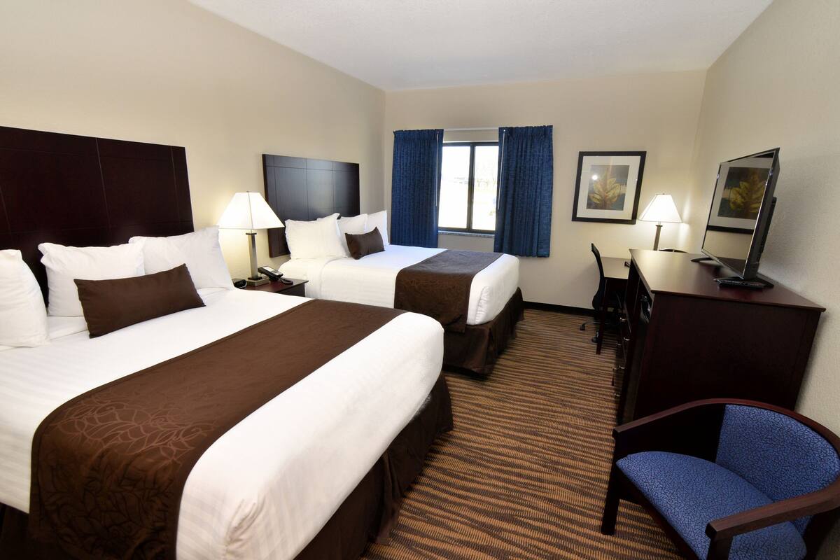 A hotel room with two beds, a desk, a chair, a TV, and a window with curtains.