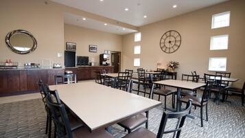 A hotel dining area with multiple tables and chairs, a kitchen area, and a large clock on the wall.