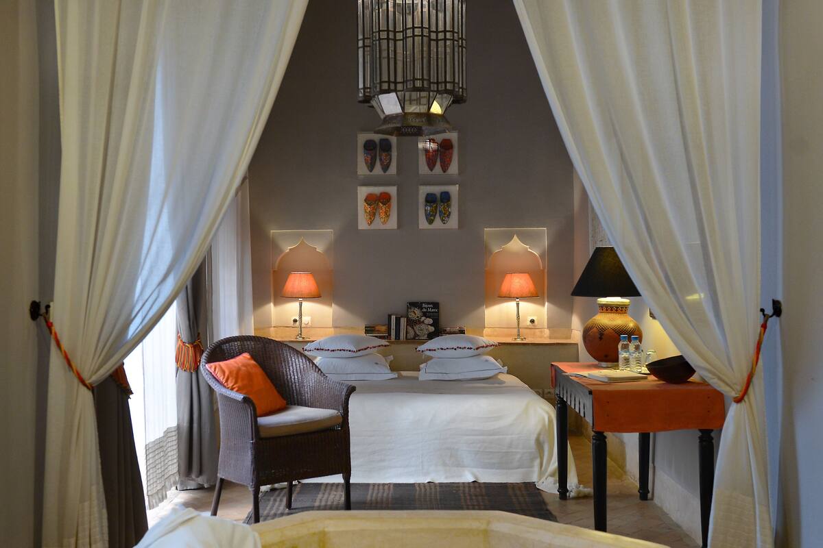 A bedroom with a bed, two bedside tables, a chair, a bathtub, and curtains.