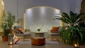 A lounge area with two cushioned chairs, a small round table, and a decorative mirror. - Dar Housnia (Marrakech)