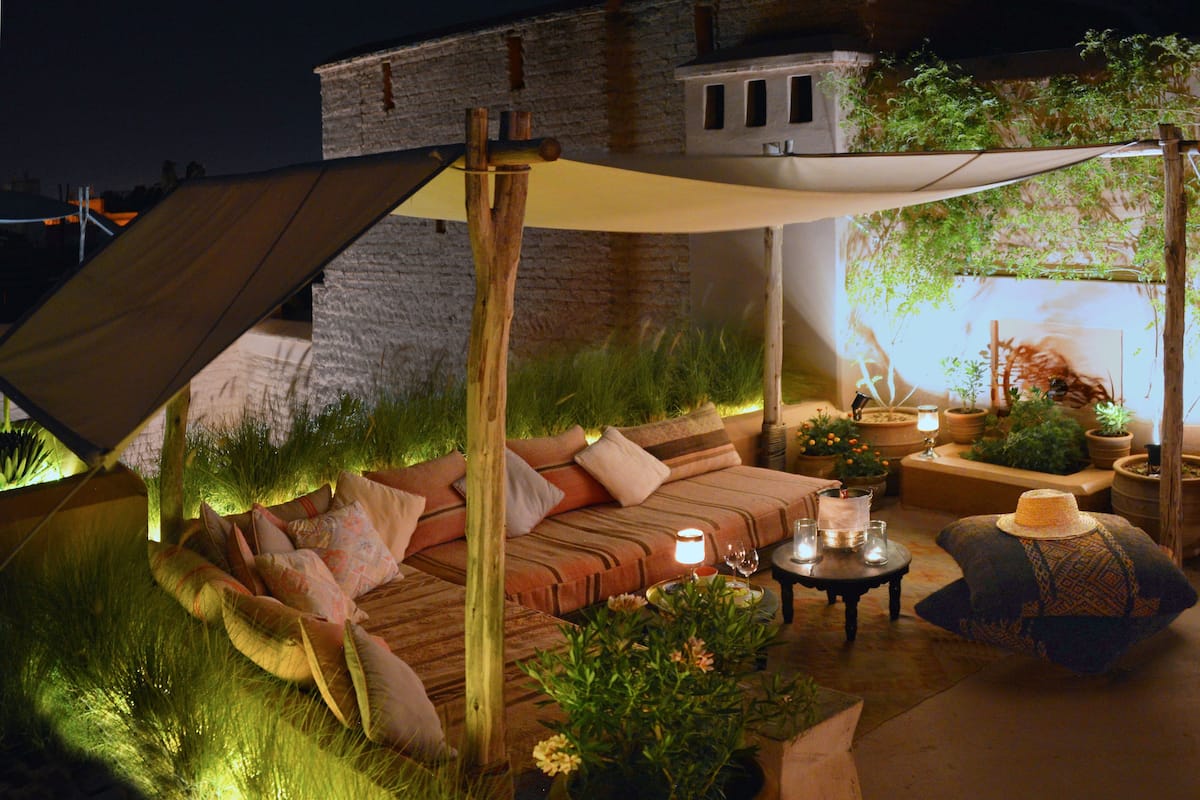 An outdoor seating area with a sofa, cushions, a table, and potted plants.