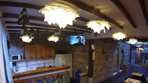 A restaurant with a bar area, wooden tables, and a television screen. - Karuss Hostel (Bogotá)